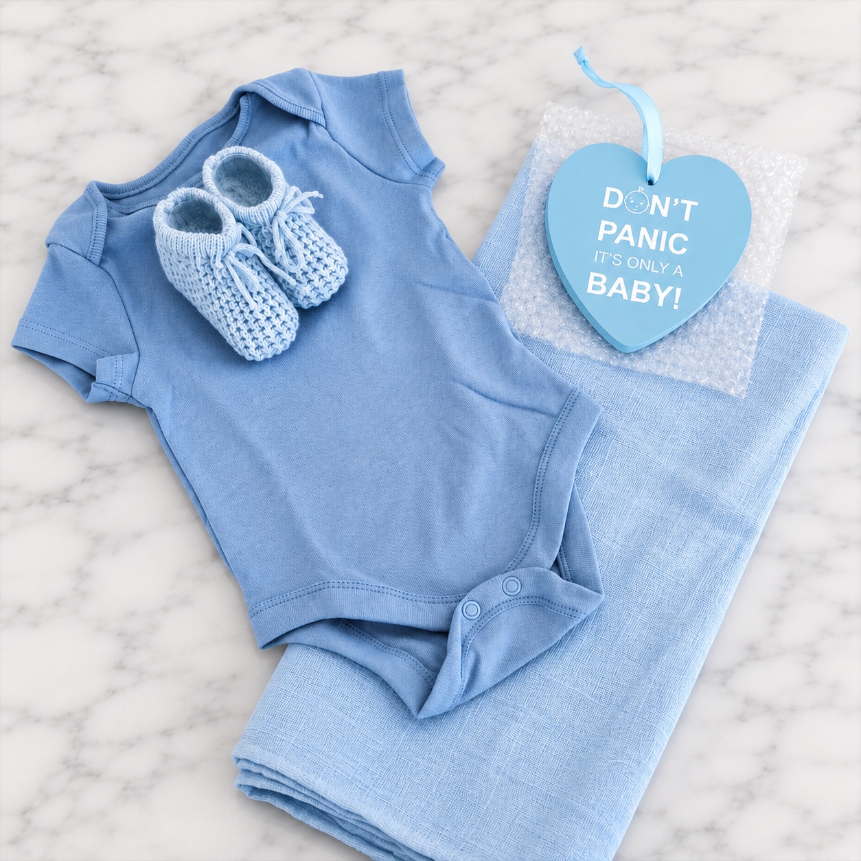 The blue nappy cake contents laid out — bodysuit, knitted booties, muslin square and the heart plaque