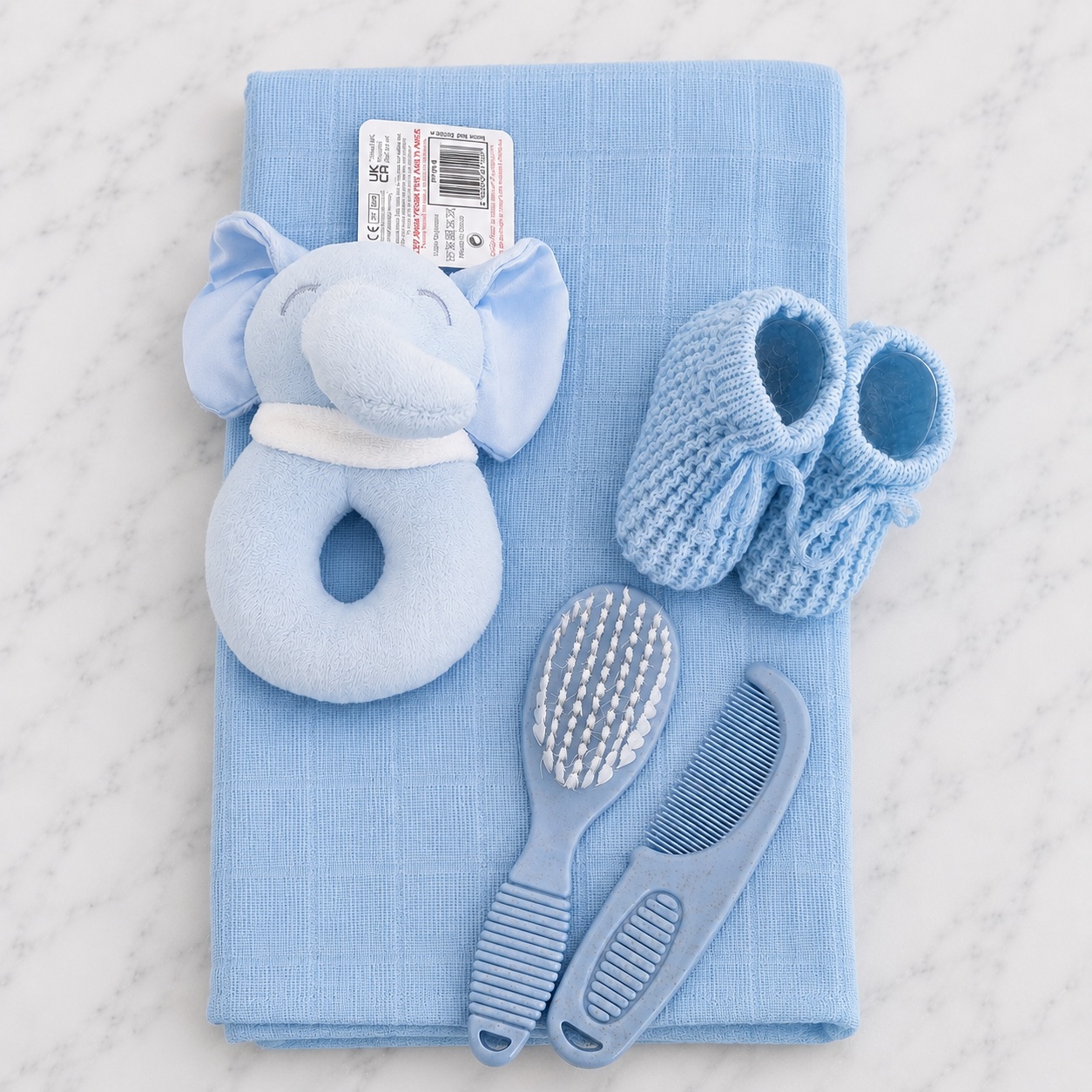 The nappy cake contents laid out — a blue elephant rattle, muslin square, knitted booties and a brush and comb set