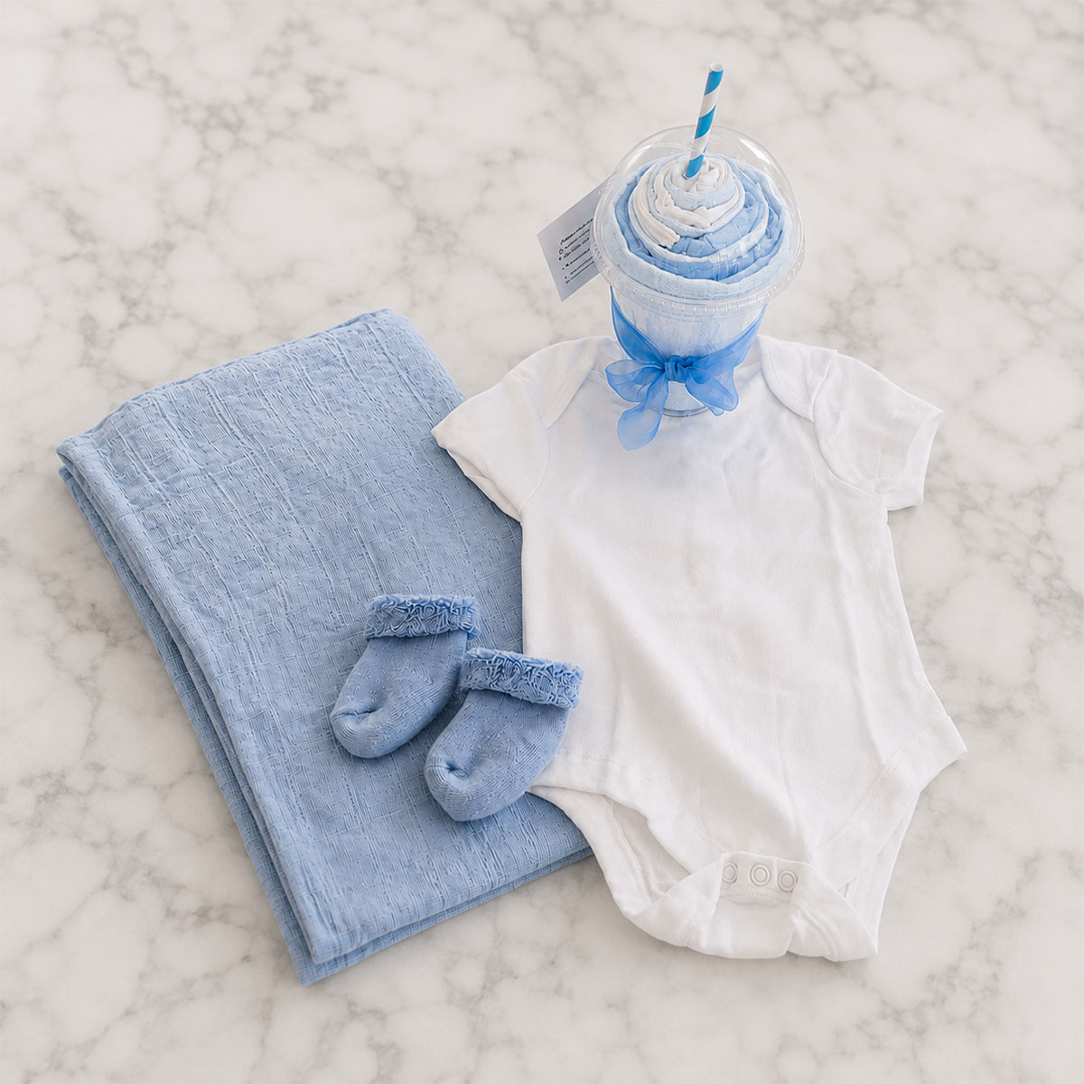 The milkshake hamper contents laid out — blue muslin, baby socks and a white bodysuit
