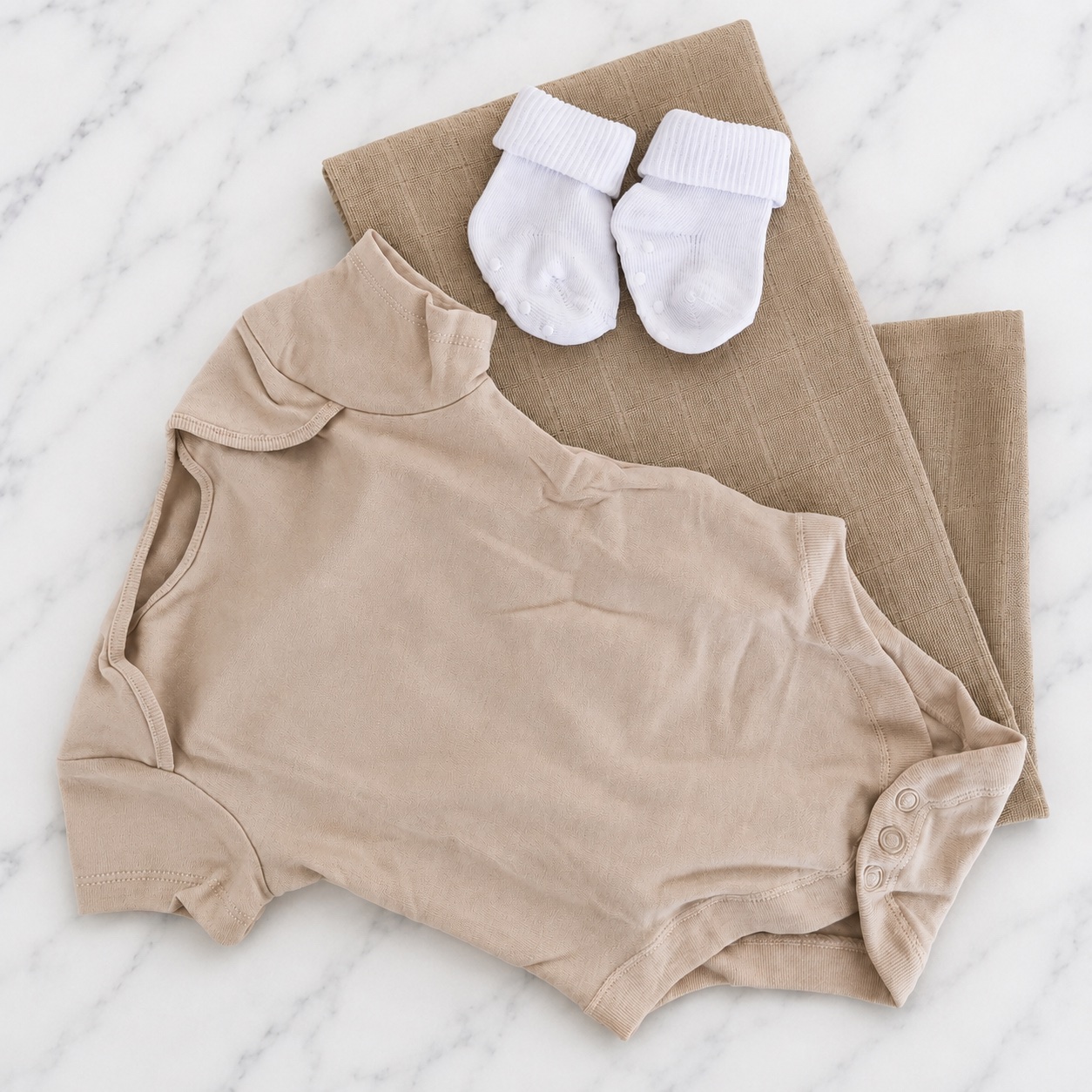 The neutral milkshake hamper contents laid out — a biscuit bodysuit, biscuit muslin square and white baby socks