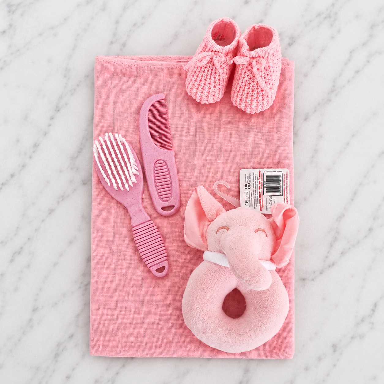 The pink nappy cake contents laid out — muslin square, knitted booties, brush and comb set and elephant rattle